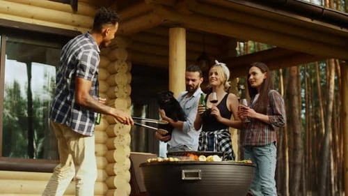 Multi ethnic friends clinking glasses at backyard grill party near forest house