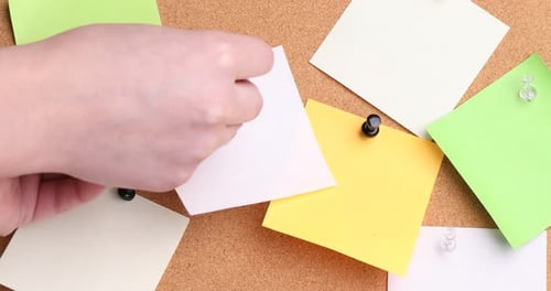 Reminder. Woman putting sticky note onto cork board, closeup