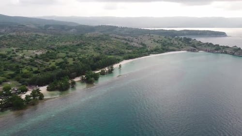 Aerial view of tropical beach and sea water with small waves close to mountains.