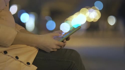 Closeup of Female Hands Holding Mobile Phone Browsing Internet on City Street with Blurred Lights at