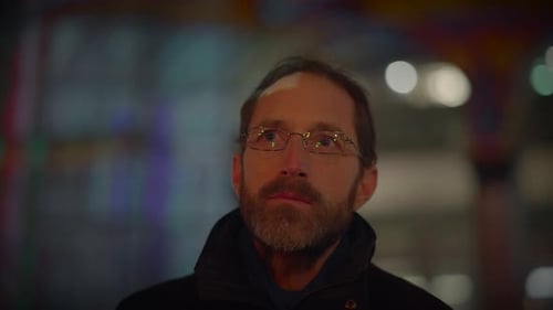 A Man in Glasses Gazes Thoughtfully Into the Night in a City Evoking Contemplation and Serenity