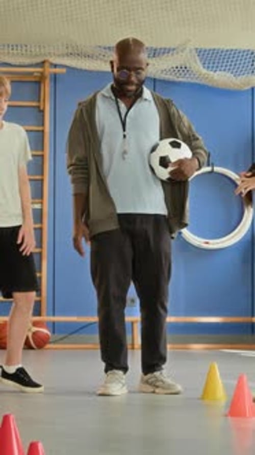 Adult and children in school gym with soccer ball