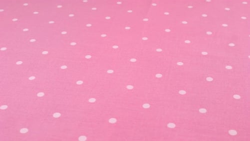 Close-up view of the orchid pink with white polka dots cotton fabric rotated on the display case.