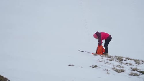 Woman in pink coat and hat checking equipment while standing in snow. Mountain climbing preparations