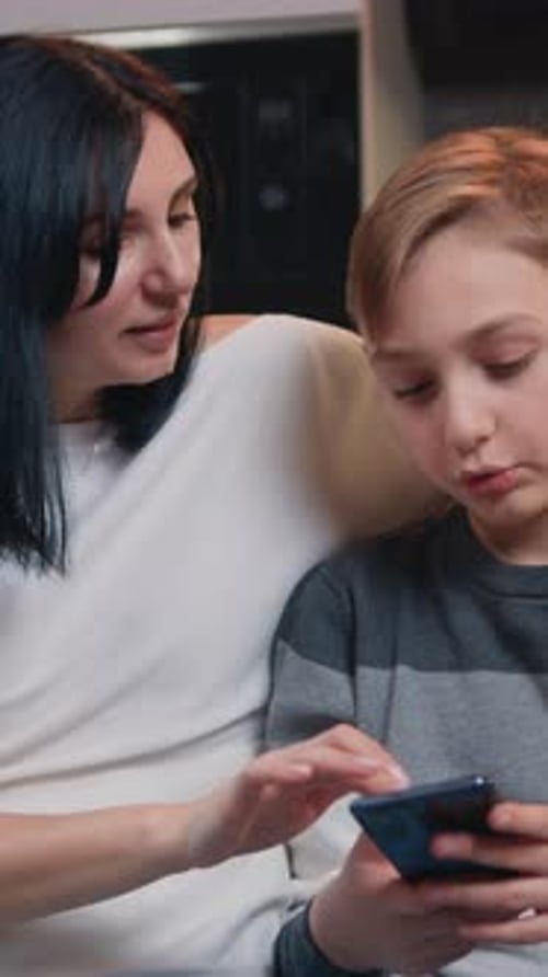 Mother and Boy Use Phone Together Indoors