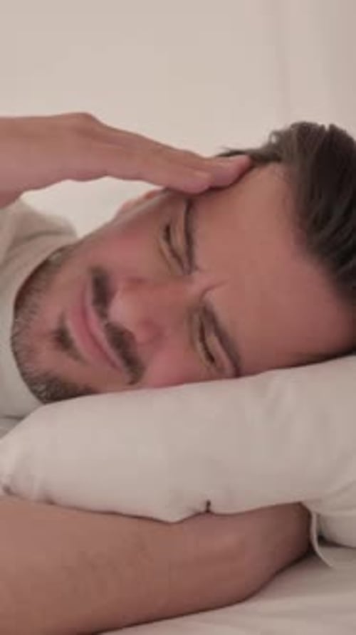 Junger Mann mit Kopfschmerzen liegt auf der Seite im Bett, vertikales Video
