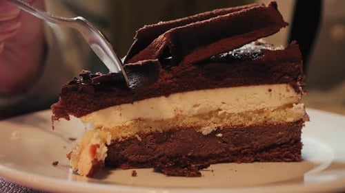 A delicious slice of layered chocolate and cream cake on a white plate in a cozy cafe setting.
