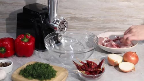 Woman making minced meat with electric grinder at grey table in kitchen, closeup