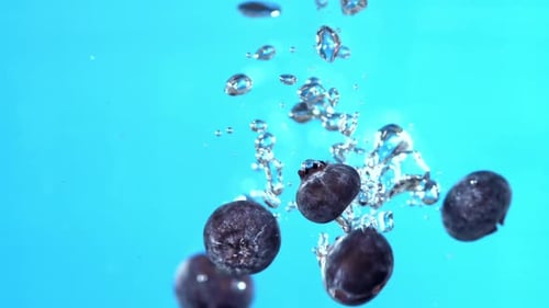 Blueberries Splashing Into Water on Blue Background