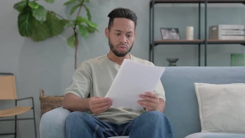Worried Man Reading Documents on Couch Indoors