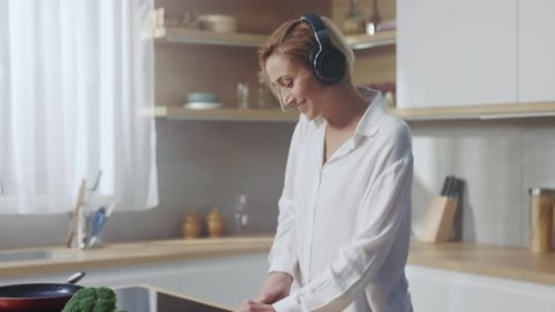 Woman with Headphones Cuts Vegetables in Modern Kitchen