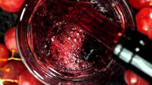 Pouring Red Wine into Glass with Red Grapes