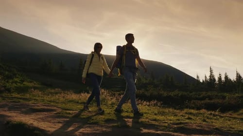 Young Couple of Tourists Holding Hands Walking Along a Mountain Path in the Rays of the Setting Sun
