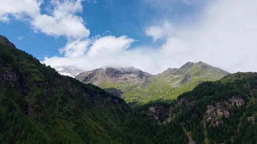 High Mountain Peaks and Lush Green Slopes Under a Blue Cloudy Sky
