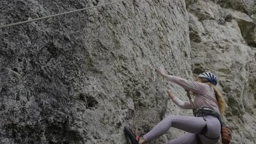 Athletic Woman Climber with Safety Helmet and Harness is Scaling a Steep Rock Face Demonstrating