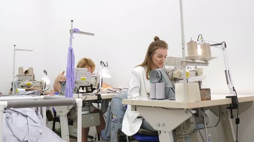 Eine junge Frau näht Kleidung in einer Lichtwerkstatt hinter einer Nähmaschine