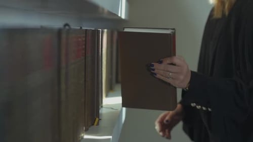 Woman Lawyer pulls a book from the shelf of the library in her office. browsing the pages of the boo