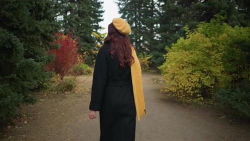 Back View of Young Woman Strolling Through Vibrant Autumn Park in Yellow Beret and Scarf