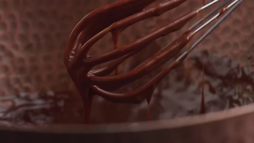 Köstliche geschmolzene Schokolade, die aus dem Schneebesen fließt, ein Gourmet-Dessert-Topping
