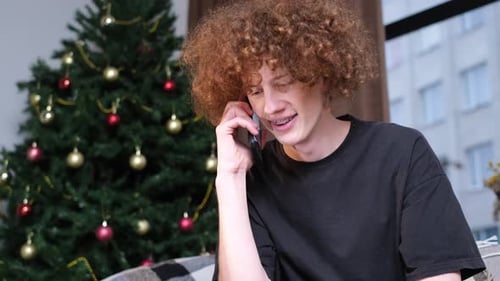 Young Adult Talking on Phone Near Christmas Tree