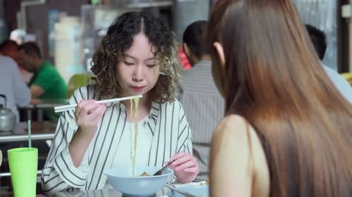 Women eating noodles together at a casual outdoor restaurant
