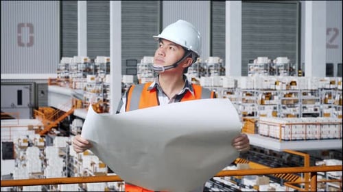 Asian Male Engineer Looking At Blueprint And Looking Around The Warehouse