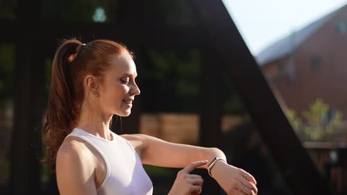Side View of Smiling Female Runner Looking Smart Watch at Modern Track Positive Sporty Jogger Using