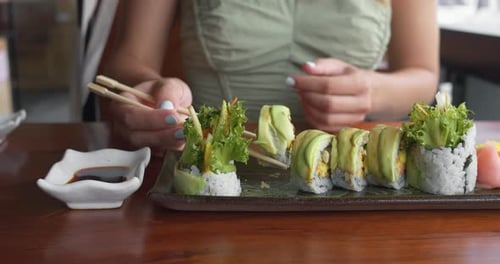 Eating Sushi in Restaurant with Chopsticks Woman Enjoys Dinner Lunch in Restaurant Eats Green Sushi