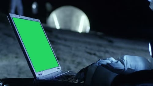 Un astronaute de la planète extraterrestre travaille sur une maquette d'ordinateur portable à écran vert. En arrière-plan, Her Crew Me