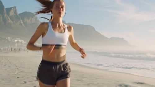 Fitness, health and exercise of active, athletic female running along the beach with earphones