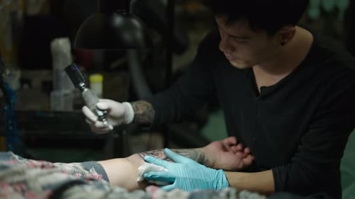Asian Tattoo Artist Using Vaseline in a Client Arm