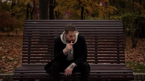 homme fume une cigarette Électronique dans le parc assis sur un banc - printemps