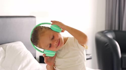 Little Girl Enjoying Music Using Green Kids Headphones in Home Bed