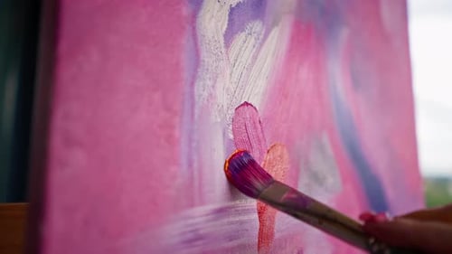 Close-up of a girl artist with a brush applying oil paint to a painting standing on an easel studio