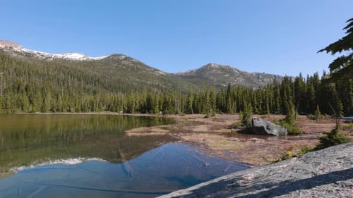 Grandes rocas y árboles en la orilla pantanosa de un lago alpino en las montañas de Washington. Disparado