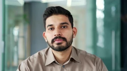 Portrait of a serious bearded entrepreneur in a shirt sitting at workplace in a business office.
