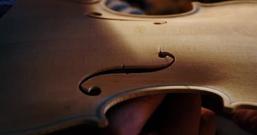 Slow motion macro of master artisan luthier painstaking detailed work on wood violin in a workshop