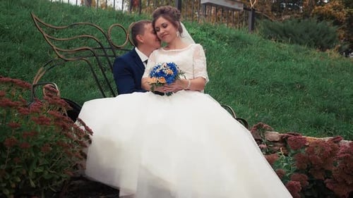 A Happy Young Couple is Sitting on a Bench in the Middle of a Beautiful Green Park on a Warm Summer