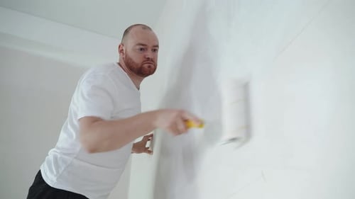 Young man paints the wall with a roller with white paint. the concept of home renovation, renovation