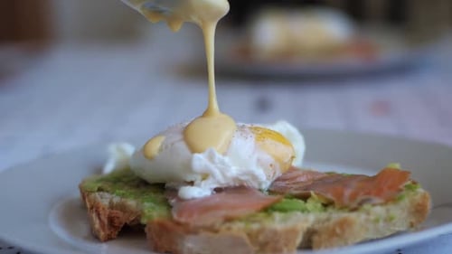 Pouring Hollandaise sauce into Benedict eggs with smoked salmon and avocado, Tasty Breakfast