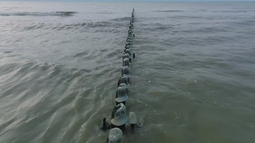Aerial birdseye view of an old wooden pier at the Baltic sea coastline, overcast winter day, white s