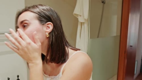Woman Applying Lotion in Bathroom Mirror