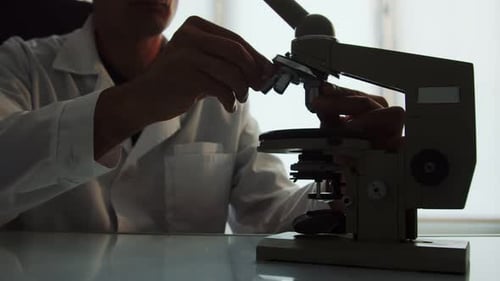 Scientist Adjusting Settings on Microscope in Laboratory
