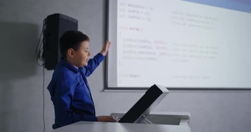 Schüler spricht vor Klassenkameraden im Klassenzimmer und präsentiert seinen Programmcode