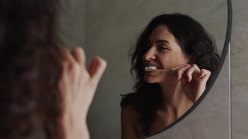 Woman Brushing Teeth in Bathroom Mirror