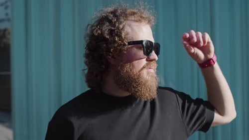 Smiling Man Lowers Sunglasses Near Corrugated Metal Wall