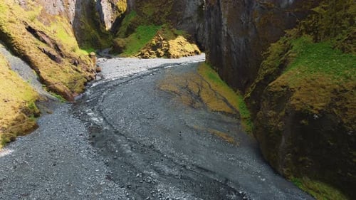 The aerial view of a hiker walking on stones at the bottom of a ravine with steep cliffs. Stakkholts