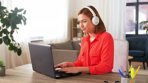 Young Woman Working on Laptop Wearing Headphones at Home