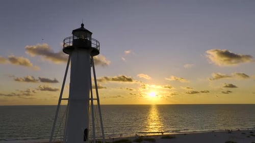 White Tall Lighthouse on Sea Shore Against Yellow Sunset Sky for Commercial Vessels Navigation
