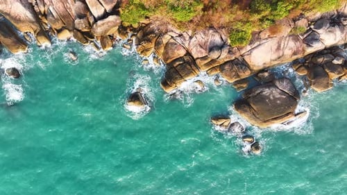 Aerial drone view of foamy waves breaking on a rocky shore. Sea crashing on rocky shore.